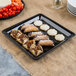 A Fineline black plastic square catering tray with food on it on a table in a bakery display.