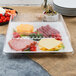 A Fineline white plastic square catering tray with meat, cheese, and vegetables on a table.