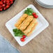 A Fineline white rectangular plastic catering tray with bread sticks and cherry tomatoes on it.