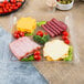 A Fineline clear plastic square catering tray with sliced ham, cheese, and vegetables.