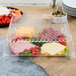 A Fineline clear plastic square catering tray with food inside.