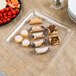 A Fineline clear plastic square catering tray with food on it on a table.
