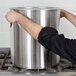 A person using a Vollrath stainless steel cover on a large pot on a stove.