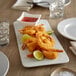 A white plate of fried shrimp with lime wedges and red sauce.