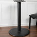 A BFM Seating black stamped steel table base on a wood floor.