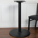 A black BFM Seating stamped steel table base with a white top on a table with a black chair.