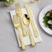 A Visions gold plastic cutlery set with extra forks on a napkin next to a plate of salad.