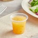 A clear plastic Choice portion cup of orange liquid next to a plate of salad.
