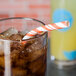 A glass of iced tea with a Sunkissed Orange and white striped paper straw on a table.