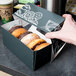 A hand holding a 9" x 4 1/2" x 4" Auto-Popup Window Cake / Bakery / Donut Box with a drawing of donuts on it.