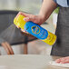 A hand spraying SC Johnson Pledge dust and allergen furniture spray on a table.