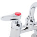 A T&S chrome deck-mounted faucet with lever handles with red buttons.