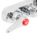 A chrome T&S wall mount faucet with lever handles and a red button on the side.