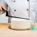 A person using a Matfer Bourgeat offset spatula with a white handle to cut a white cake.