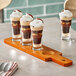 An Acopa dual-sided wooden tasting paddle with flared pilsner glasses filled with layered desserts.