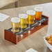 A wooden tray with four Acopa Write-On Flared Pilsner Tasting Glasses on a table with Chex Mix.