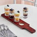 An Acopa Mahogany Finish drop-in flight paddle with pub tasting glasses holding a row of desserts on a table.