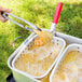 A person using tongs to fry chicken in a Backyard Pro dual basket fryer.