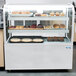 A bakery display case with pastries and an Avantco LED lamp inside.