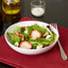 A white Carlisle melamine bowl filled with salad with strawberries, walnuts, and almonds.