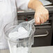 A person using a Rubbermaid clear plastic bar scoop to add ice to a blender.