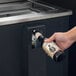 A hand opening a bottle of beer and pouring it into an Avantco black horizontal bottle cooler.