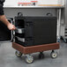 A man uses a Cambro dark brown Camdolly to transport Cambro food containers.