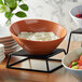 A pumpkin slanted melamine bowl on a stand filled with food.