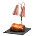 A close-up of a piece of meat being carved under a shiny bright copper heat lamp.