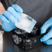 A person in blue gloves pouring ice into a black American Metalcraft silicone ice mold.