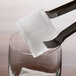 A pair of tongs pulls a black Tablecraft silicone ice cube from a glass.