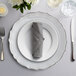 A table set with a Scalloped White Alabaster Glass Charger Plate with silverware and a napkin.