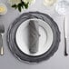 A table set with a black and silver scalloped charger plate, silverware, and a napkin.
