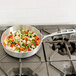 A Vollrath Wear-Ever saute pan filled with vegetables on a stove.