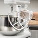 A person wearing white gloves attaches a white KitchenAid flat beater to a mixer.