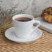 A Libbey Ultra Bright White porcelain espresso cup of coffee on a saucer next to a pastry.