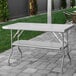 A Regency stainless steel folding work table with a metal bar on a brick patio.