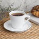 A Libbey white porcelain espresso saucer with a cup of coffee and a pastry on a table.