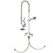 A T&S chrome deck mounted pre-rinse faucet with lever handles and a hand sprayer.