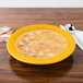 A yellow Fiesta china rim soup bowl filled with soup on a table with a spoon.