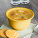 A Fiesta china bouillon bowl filled with soup next to a cracker on a table with a spoon.