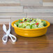 A Fiesta white china bowl filled with salad on a wood table with a pair of scissors.