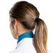 A woman in a white chef coat and teal chef neckerchief with her hair in a ponytail.