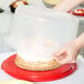 A person holding a Rubbermaid plastic container lid over a white cake.