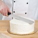 A hand holding a black Ateco baking spatula cutting a cake.