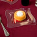 A Fineline clear plastic square plate with a small round pastry topped with whipped cream and strawberries.