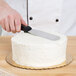 A hand holding an Ateco straight spatula with a black plastic handle over a cake.