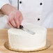 A person using an Ateco straight baking / icing spatula with a plastic handle to cut a cake.