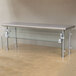 A long silver metal table with a stainless steel Advance Tabco food shield with glass panels.