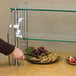A person using an Advance Tabco food shield to protect a buffet of cookies, grapes, and chocolate covered strawberries.
